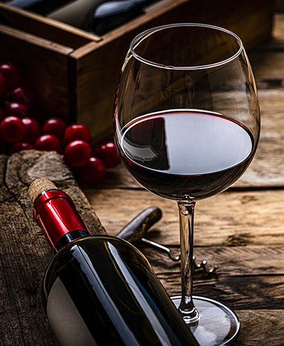 Glass of red wine next to bottle of wine on its side on a wooden table.