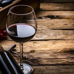 Glass of red wine next to bottle on its side on wooden table.