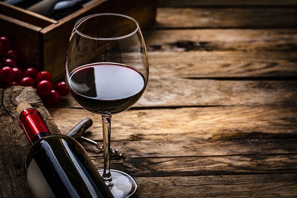 Glass of red wine next to bottle on its side on wooden table.